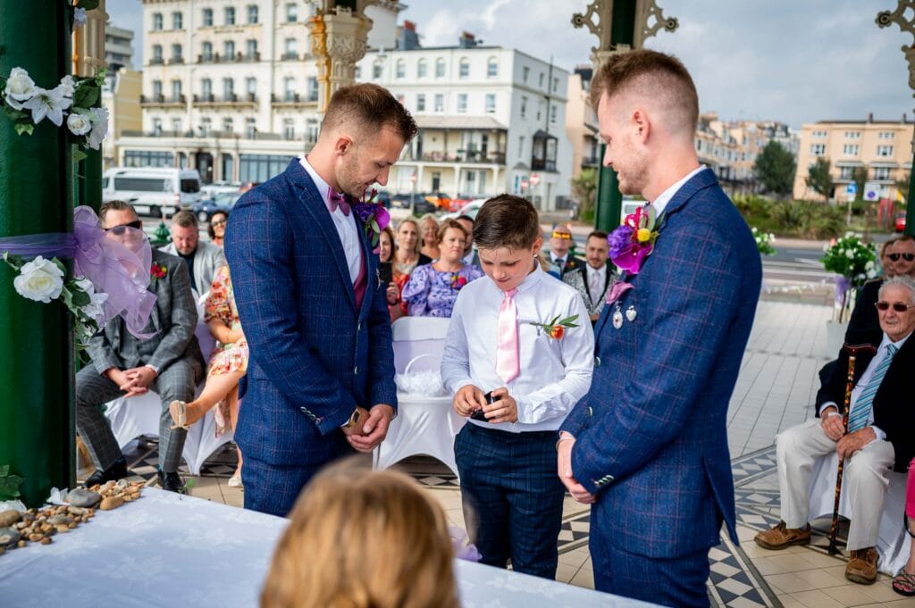 Ring bearer gives rings to two grooms at Brighton Bandstand