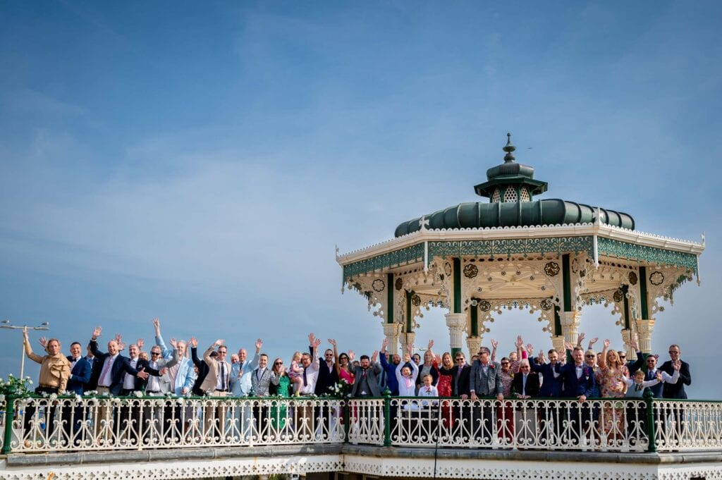 Wedding group photo of guests waving at Brighton Bandstand