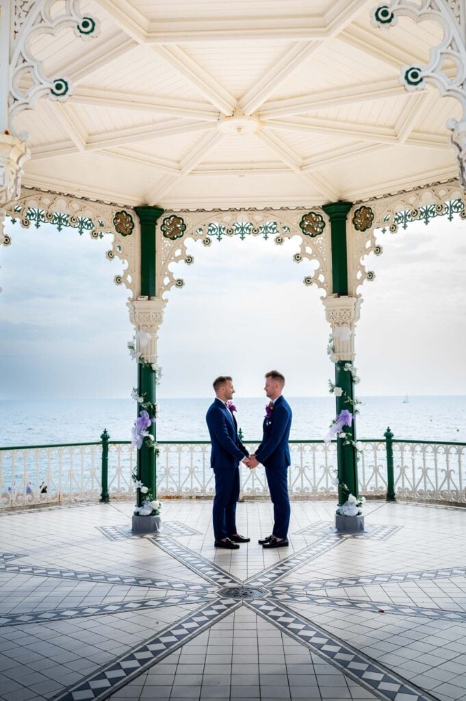 Loving grooms holding hands at Brighton Bandstand